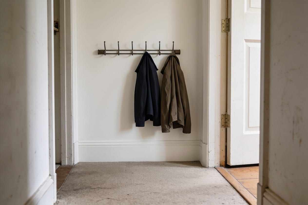 The same wall smooth and freshly painted, with the coat rail fixed straight and coats hanging on it