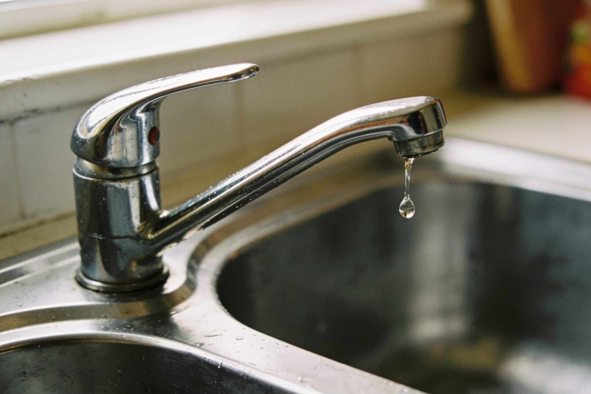 A single drop falling from a chrome kitchen tap into a sink